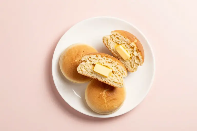 Three Belizean johnny cakes are stacked on a white plate, split open to show tender crumb and melting butter.