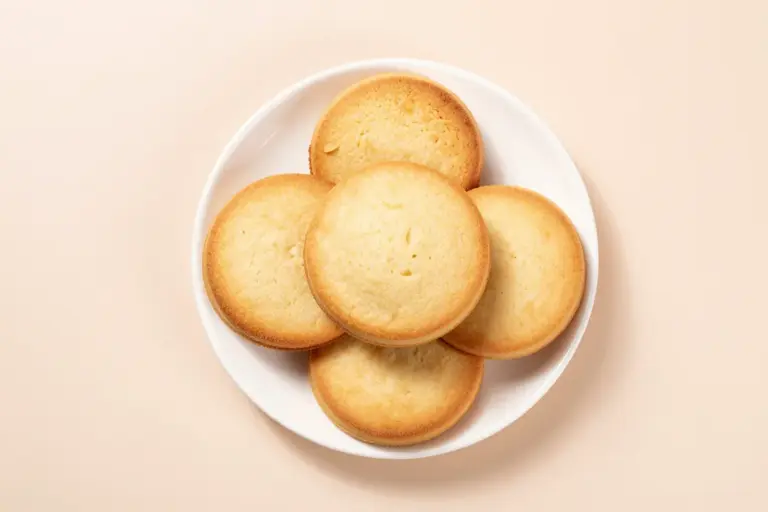 Five Belizean journey cakes stacked on a white plate, showing fork-pricked golden tops.
