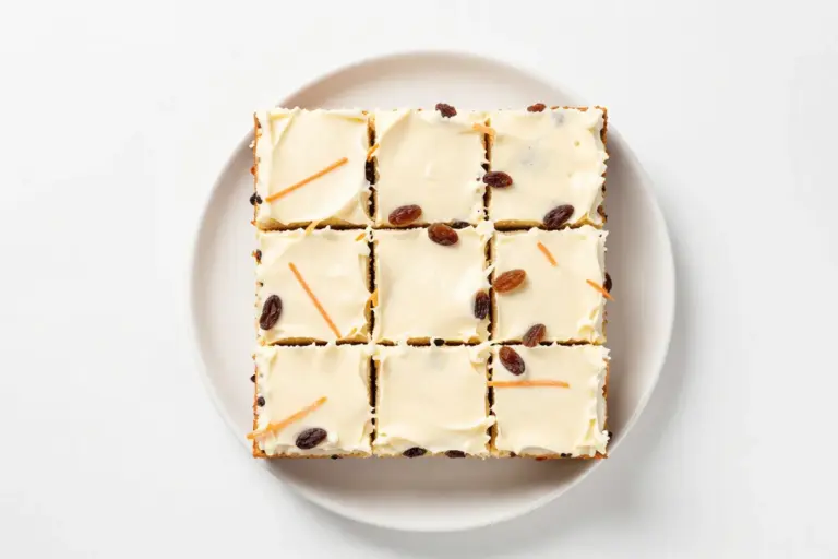 Neat squares of carrot cake with raisins and cream cheese frosting on a white ceramic plate
