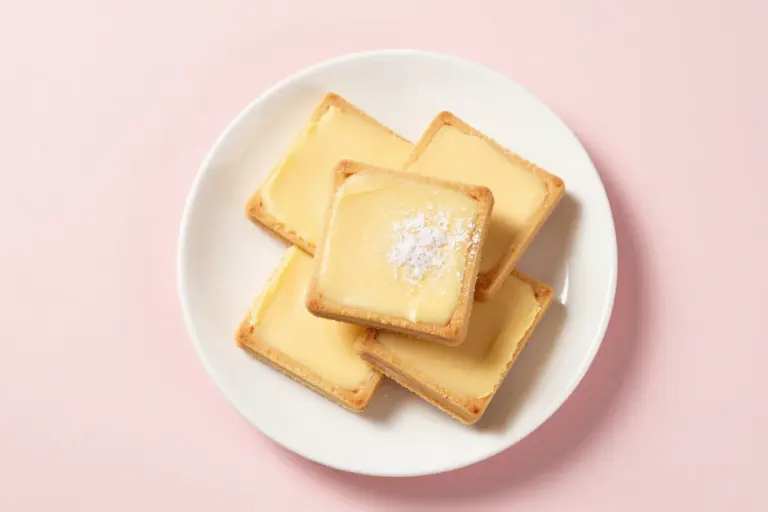 Stacked chess squares with a buttery golden crust and pale-yellow cream cheese topping on a white plate