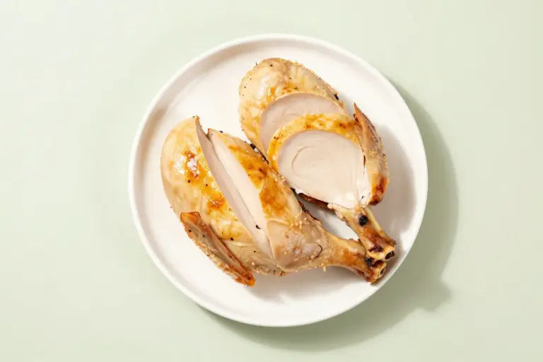 Sliced roasted chicken breast on a white plate against a pale sage background.