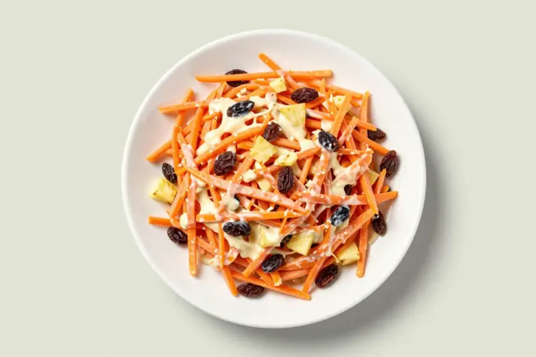 Finely shredded carrot raisin salad with pineapple pieces in a creamy dressing on a white plate.