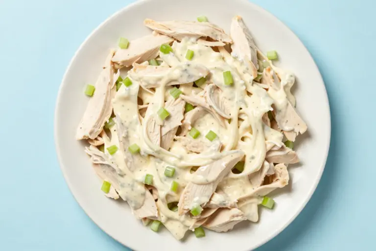 Creamy chicken salad with finely diced celery served on a white ceramic plate against a pale blue background