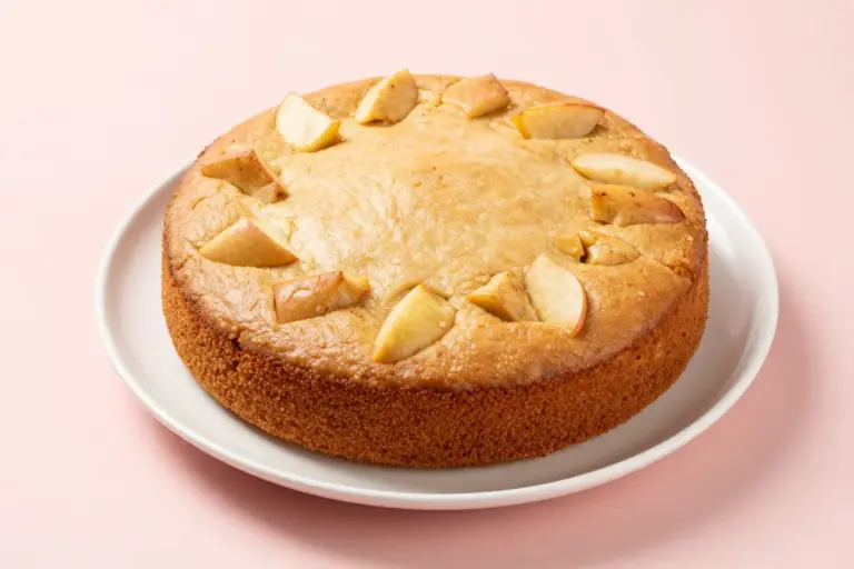 Whole dairy-free apple cake with diced apples on a white ceramic plate