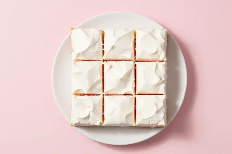 Chilled soda poke cake squares with pink syrup channels and smooth white vanilla topping on a white plate.